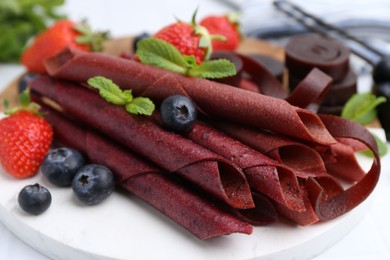 Photo of Tasty fruit leather rolls, strawberries, blueberries and mint on white table, closeup