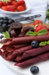 Photo of Tasty fruit leather rolls, strawberries, blueberries and mint on white table, closeup