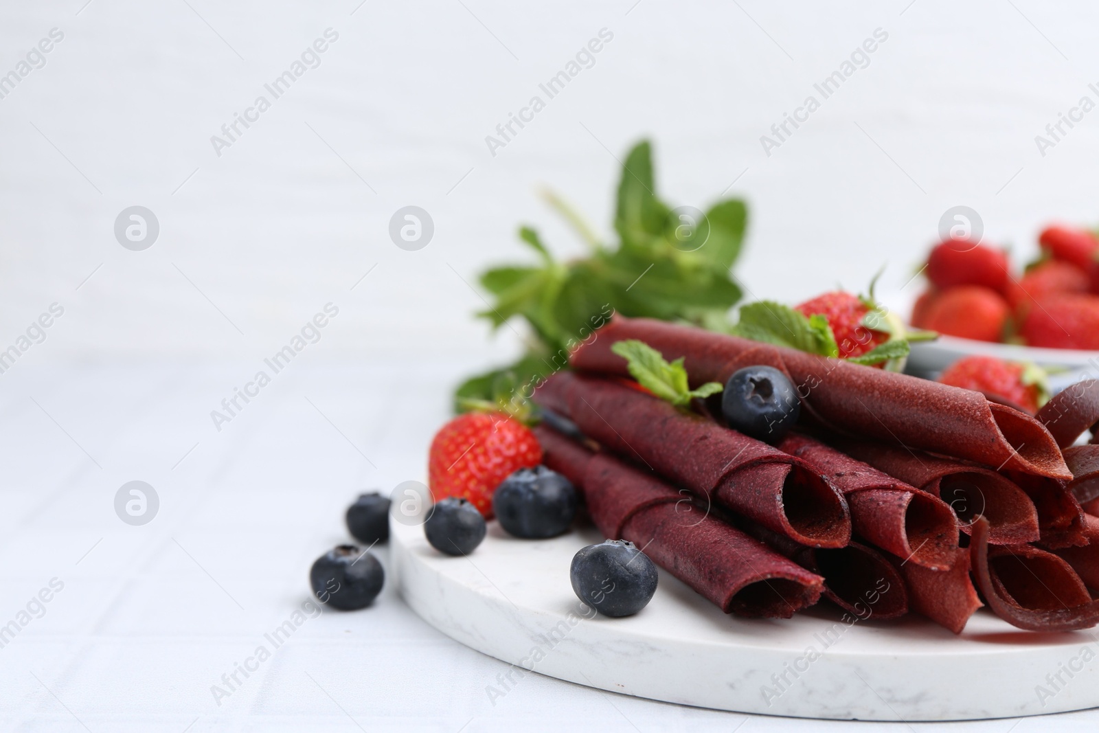Tasty fruit leather rolls, strawberries, blueberries and mint on white tiled table, closeup. Space for text Photo of Tasty fruit leather rolls, strawberries, blueberries and mint on white tiled table, closeup. Space for text