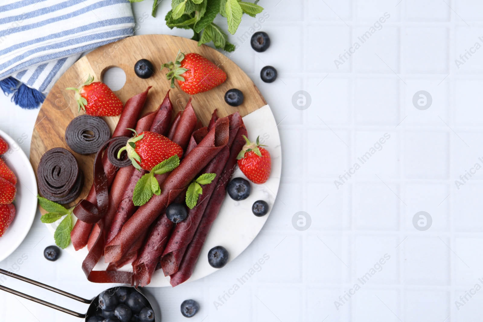 Tasty fruit leather rolls, strawberries, blueberries and mint on white tiled table, flat lay. Space for text Photo of Tasty fruit leather rolls, strawberries, blueberries and mint on white tiled table, flat lay. Space for text