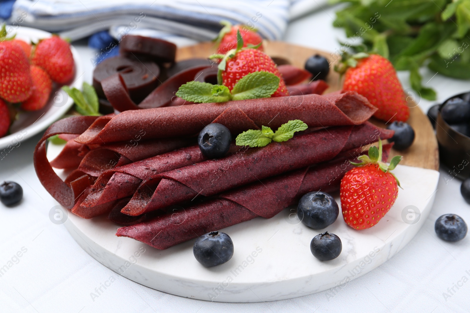 Tasty fruit leather rolls, strawberries, blueberries and mint on white table, closeup Photo of Tasty fruit leather rolls, strawberries, blueberries and mint on white table, closeup