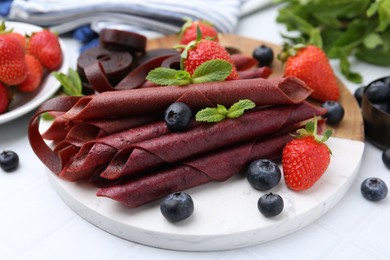 Photo of Tasty fruit leather rolls, strawberries, blueberries and mint on white table, closeup