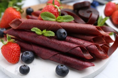 Photo of Tasty fruit leather rolls, strawberries, blueberries and mint on white table, closeup