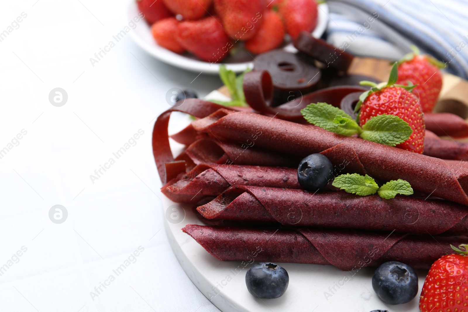 Tasty fruit leather rolls, strawberries, blueberries and mint on white table, closeup. Space for text Photo of Tasty fruit leather rolls, strawberries, blueberries and mint on white table, closeup. Space for text