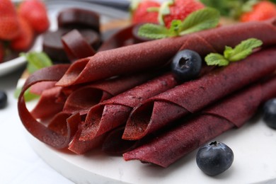 Photo of Tasty fruit leather rolls, strawberries, blueberries and mint on white table, closeup