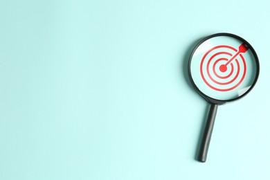 Image of Targeting. Magnifying glass with bullseye inside on light turquoise background, top view. Space for text