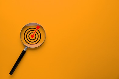 Image of Targeting. Magnifying glass with bullseye inside on orange background, top view. Space for text