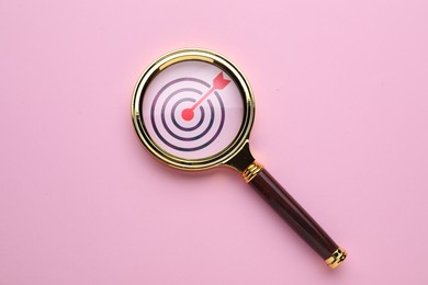 Image of Targeting. Magnifying glass with bullseye inside on pink background, top view