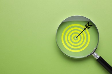 Image of Targeting. Magnifying glass with bullseye inside on light green background, top view. Space for text