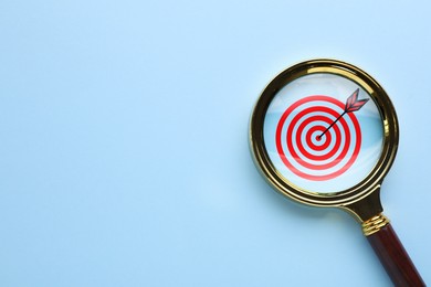 Image of Targeting. Magnifying glass with bullseye inside on light blue background, top view. Space for text