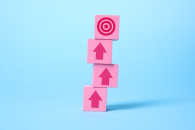 Image of Targeting. Stacked pink cubes with arrows pointing at bullseye on top cube against light blue background