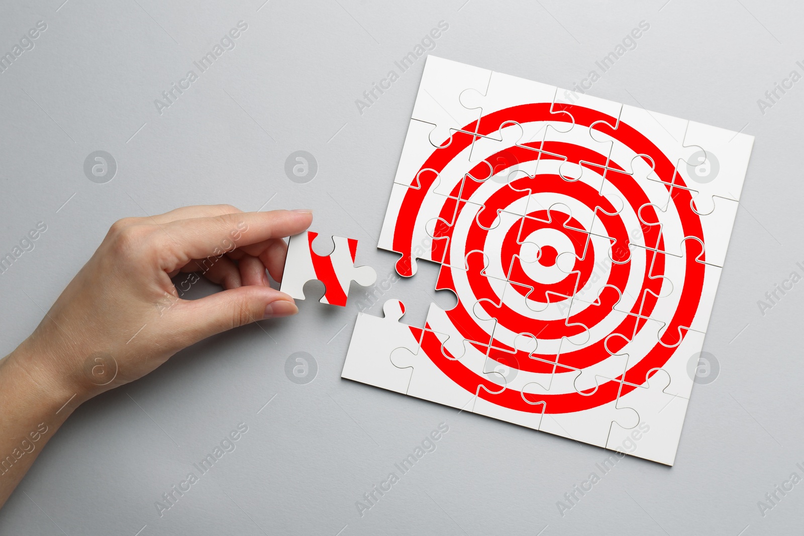 Targeting. Woman putting missing puzzle piece to make image of bullseye on light background, top view Image of Targeting. Woman putting missing puzzle piece to make image of bullseye on light background, top view