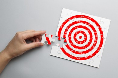 Image of Targeting. Woman putting missing puzzle piece to make image of bullseye on light background, top view