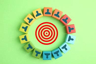 Image of Targeting. Bullseye surrounded by colorful cubes with human icons on green background, top view