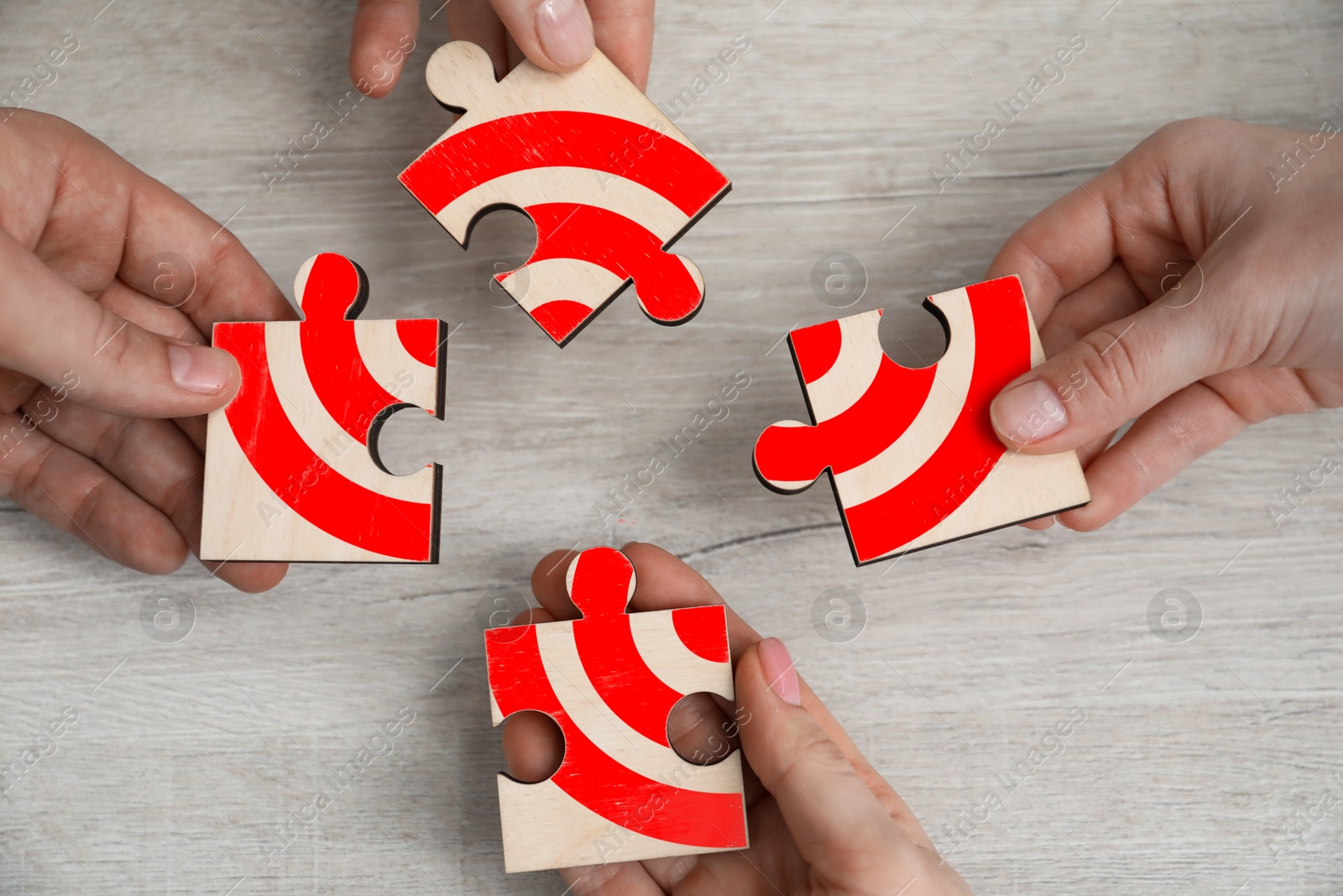 Targeting. People putting puzzle pieces together to make image of bullseye over wooden table, top view Image of Targeting. People putting puzzle pieces together to make image of bullseye over wooden table, top view