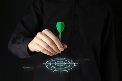 Image of Targeting. Woman aiming at center of virtual bullseye with dart on black background, closeup