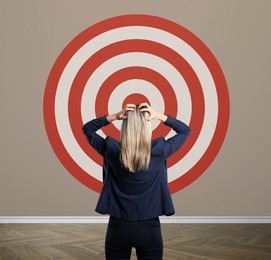Image of Targeting, goal achievement. Business woman looking at bullseye on wall indoors