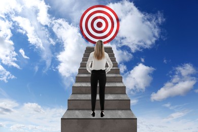 Image of Targeting, goal achievement. Business woman walking up stairs leading to bullseye in sky