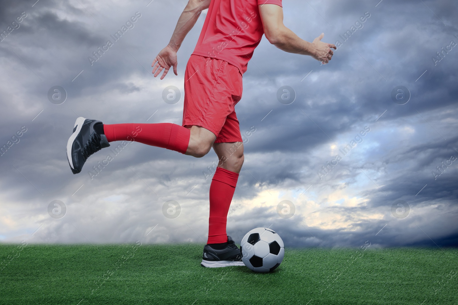 Football player kicking soccer ball under cloudy sky, closeup Image of Football player kicking soccer ball under cloudy sky, closeup
