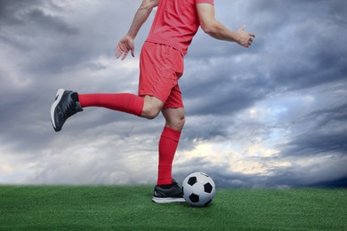 Image of Football player kicking soccer ball under cloudy sky, closeup