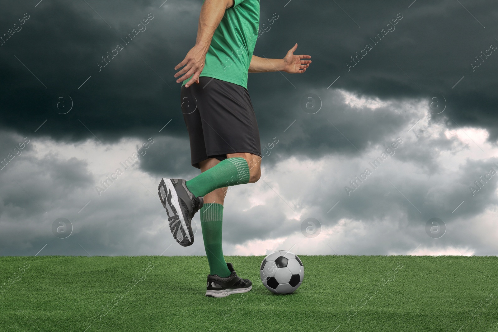 Football player kicking soccer ball under gloomy sky, closeup Image of Football player kicking soccer ball under gloomy sky, closeup