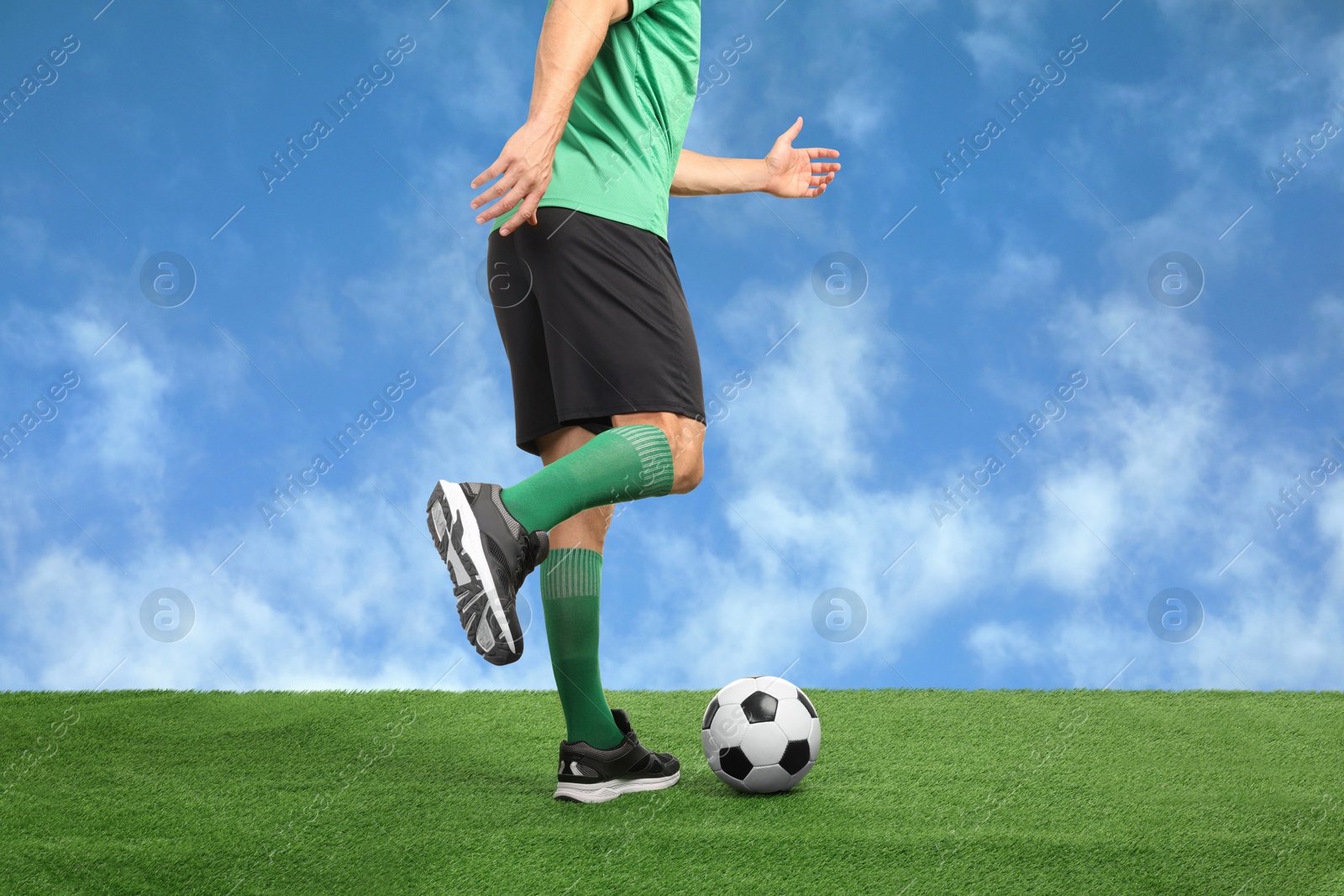 Football player kicking soccer ball under blue sky, closeup Image of Football player kicking soccer ball under blue sky, closeup