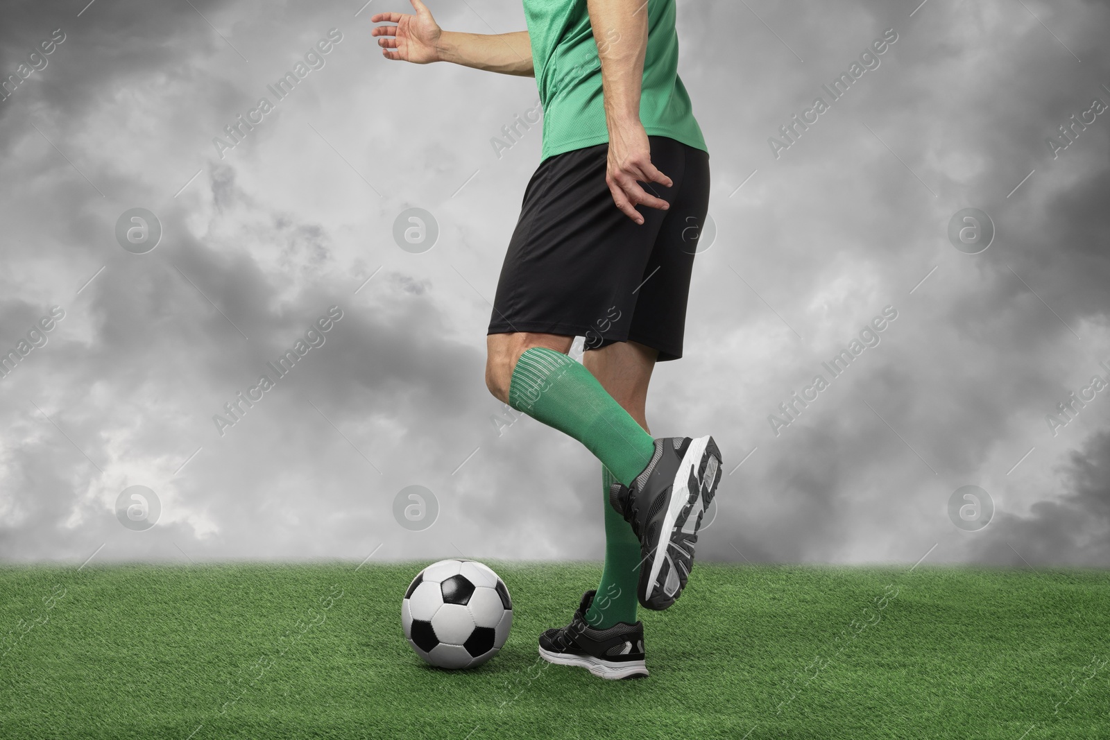 Football player kicking soccer ball under cloudy sky, closeup Image of Football player kicking soccer ball under cloudy sky, closeup
