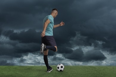 Image of Football player kicking soccer ball under gloomy sky