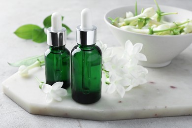 Photo of Bottles of essential oils and jasmine flowers on light grey table, closeup