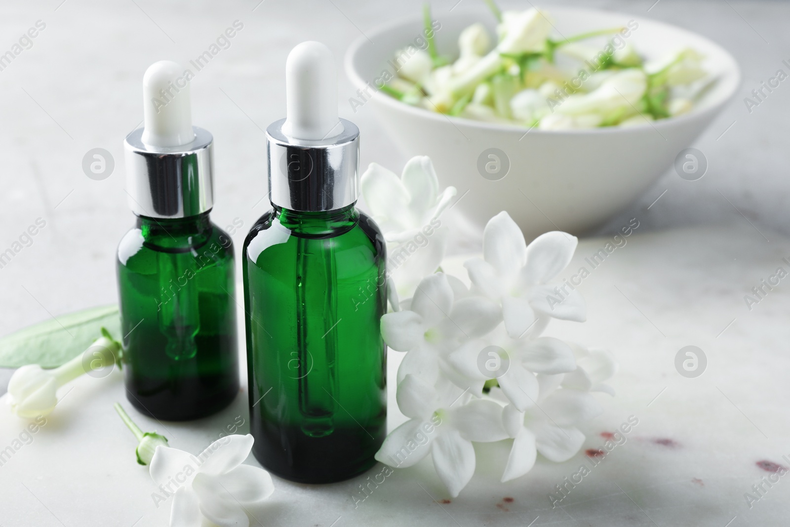 Bottles of essential oils and jasmine flowers on table, closeup Photo of Bottles of essential oils and jasmine flowers on table, closeup
