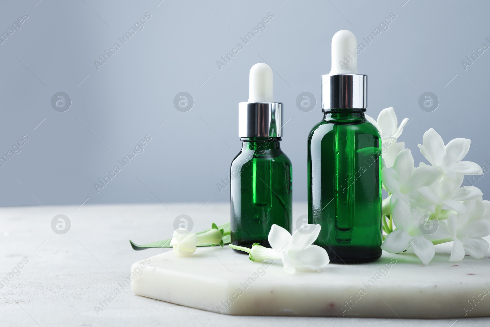 Bottles of essential oils and jasmine flowers on light grey table, closeup. Space for text Photo of Bottles of essential oils and jasmine flowers on light grey table, closeup. Space for text