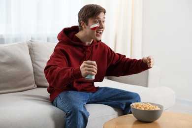 Photo of Emotional sports fan with drink and popcorn watching game at home