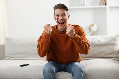 Photo of Sports fan with drawing of Italian flag watching game on sofa indoors