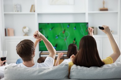 Photo of Group of football fans watching game together indoors, back view