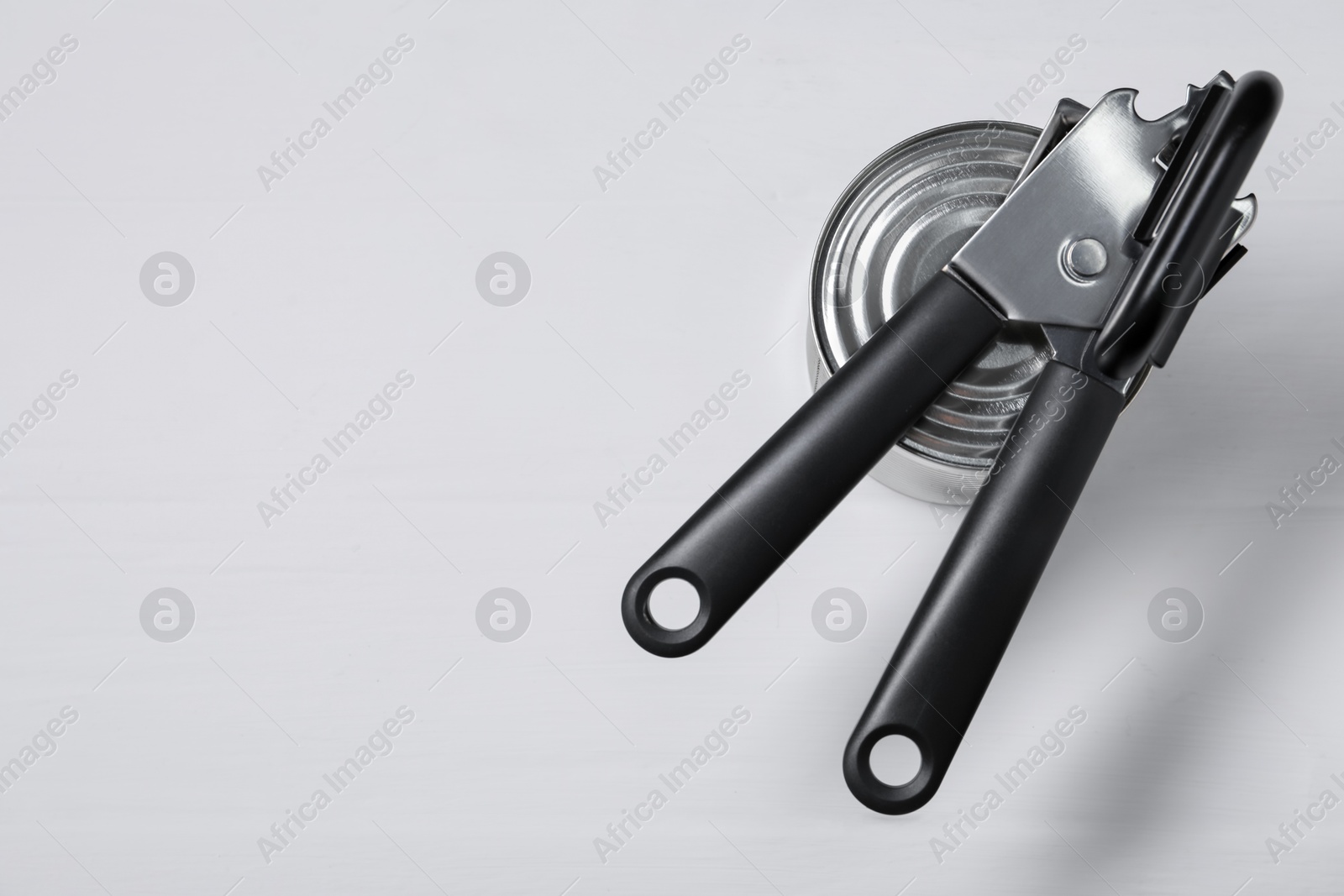 Can opener and tin on light grey table, top view. Space for text Photo of Can opener and tin on light grey table, top view. Space for text
