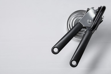 Photo of Can opener and tin on light grey table, top view. Space for text