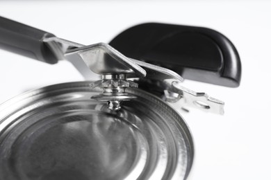 Photo of Can opener and tin on white table, closeup