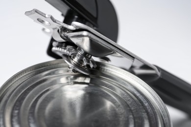 Photo of Can opener and tin on white table, closeup