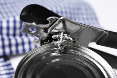 Photo of Can opener and tin on white table, closeup