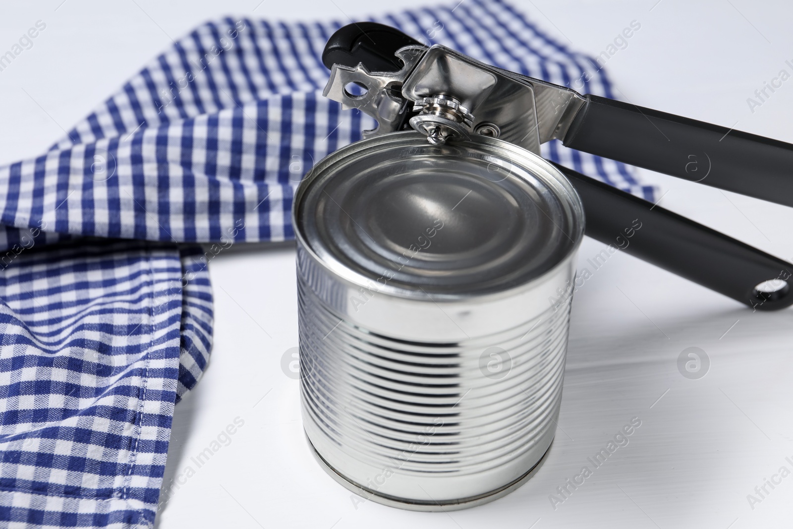 Photo of Can opener and tin on white wooden table, closeup