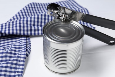 Photo of Can opener and tin on white wooden table, closeup