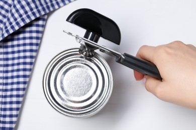 Photo of Woman opening tin with can opener at white table, top view