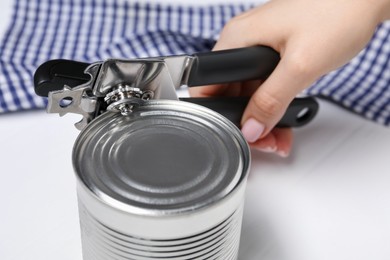 Photo of Woman opening tin with can opener at white table, closeup