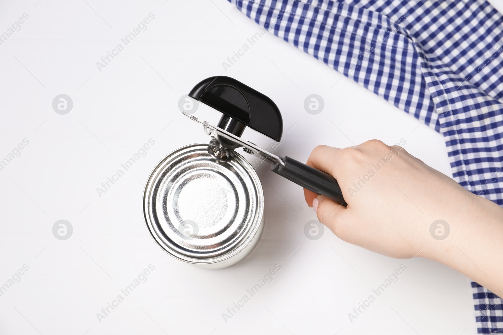 Woman opening tin with can opener at white table, top view Photo of Woman opening tin with can opener at white table, top view