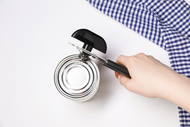 Photo of Woman opening tin with can opener at white table, top view