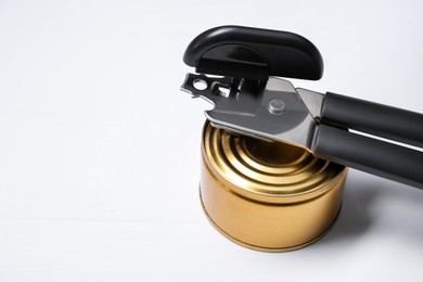 Photo of Can opener and tin on white wooden table, closeup. Space for text