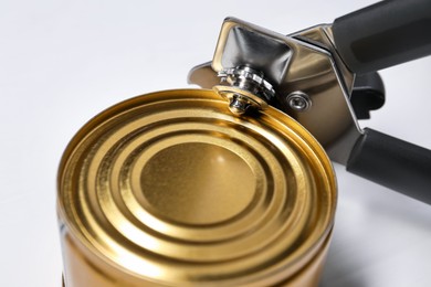 Photo of Can opener and tin on white table, closeup
