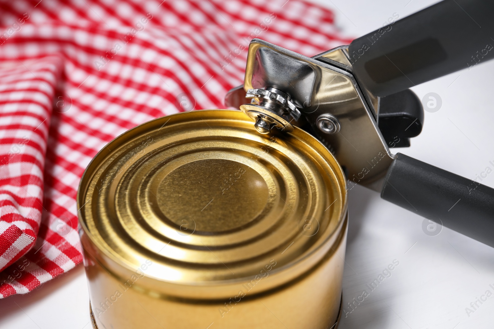 Can opener and tin on white table, closeup Photo of Can opener and tin on white table, closeup