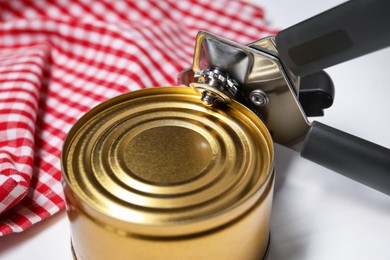 Photo of Can opener and tin on white table, closeup