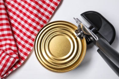 Photo of Can opener and tin on white wooden table, top view